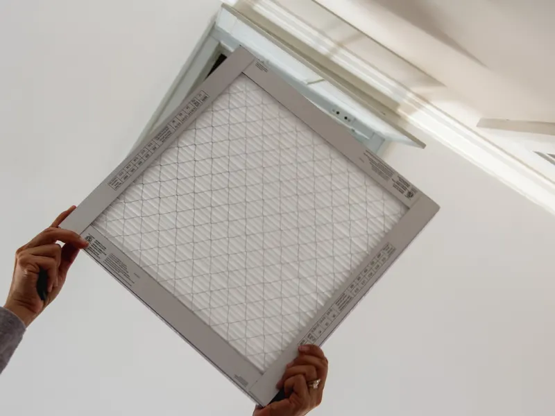 Two hands lifting a clean pleated air filter into a ceiling return vent
