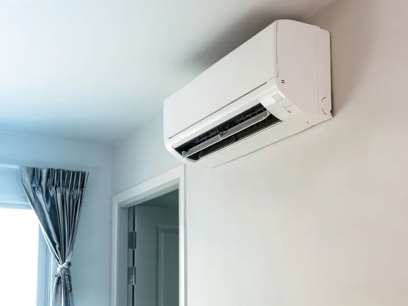 A wall-mounted ductless mini-split head installed high on an interior wall beside a curtained window