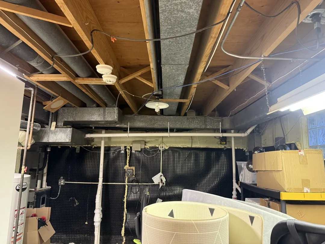 Basement ductwork before the work, with the original trunk running between the floor joists.