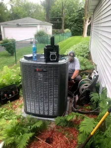 Technician working on an air conditioning unit surrounded by greenery.